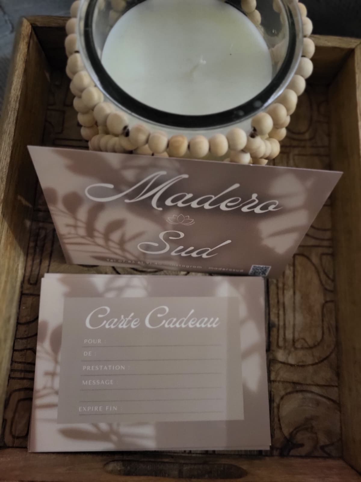 Pile de cartes cadeaux Madero Sud posées dans un plateau en bois, à côté d’une bougie.